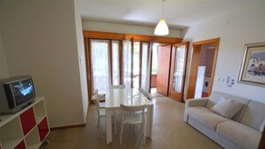 A living room with a TV, a dining table, and a sofa. - Seaside escape apartment with everything you need! (Lignano Sabbiadoro)