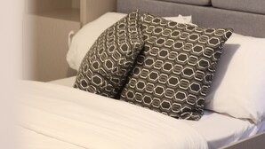 Ein ordentlich bezogenes Bett mit gemusterten Kissen, einem grauen Kopfteil und einem Regal mit Dekoration.
