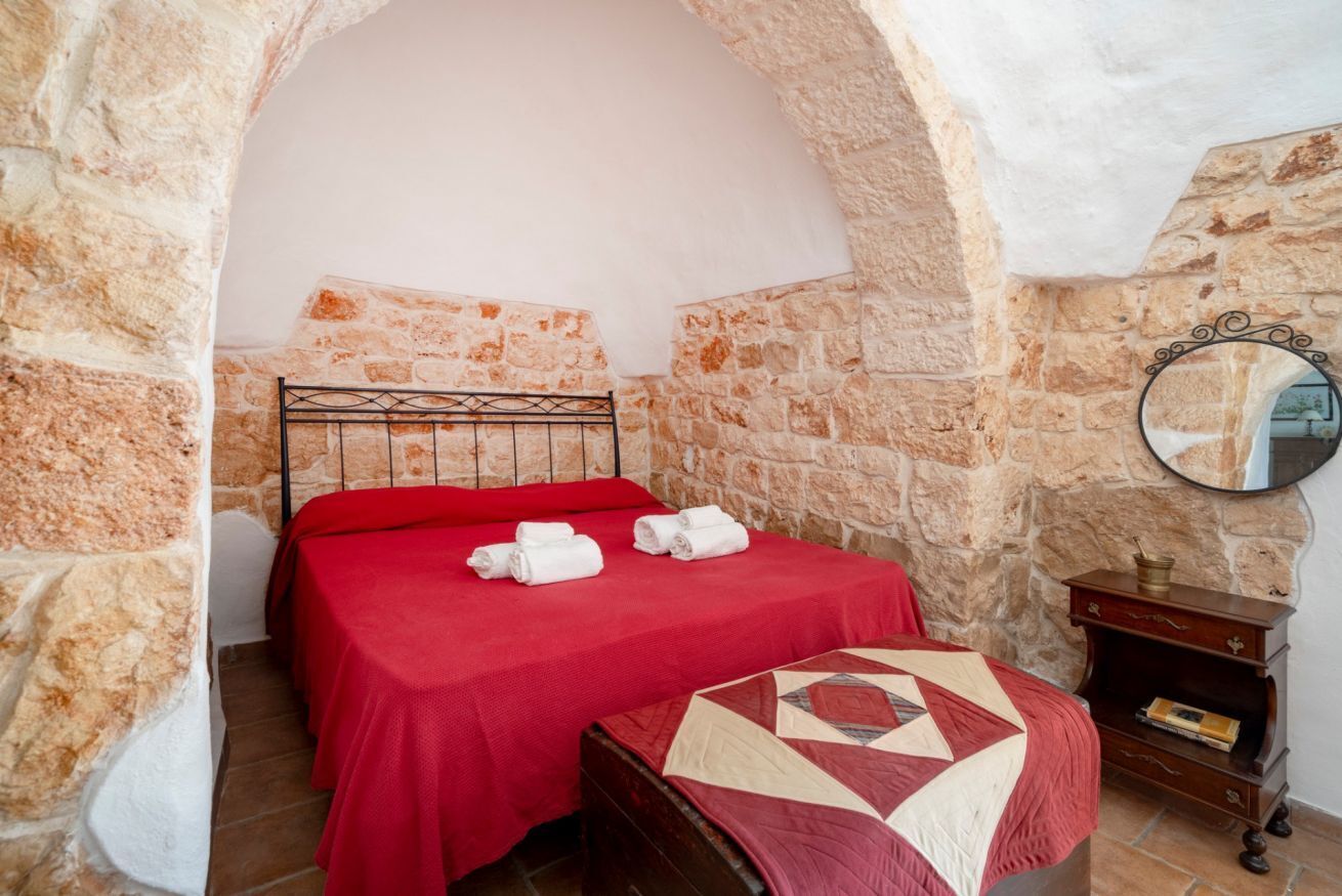 Una habitación con paredes de piedra, una cama, un colcha y una mesita de noche de madera.