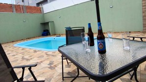 An outdoor patio area with a pool, a table with bottles and glasses, and a white object on the ground.