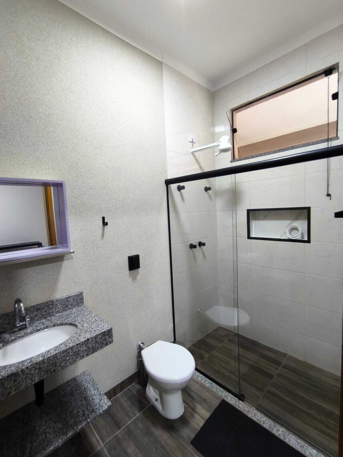 A modern bathroom with a granite countertop sink, a white toilet, and a glass-enclosed shower area.