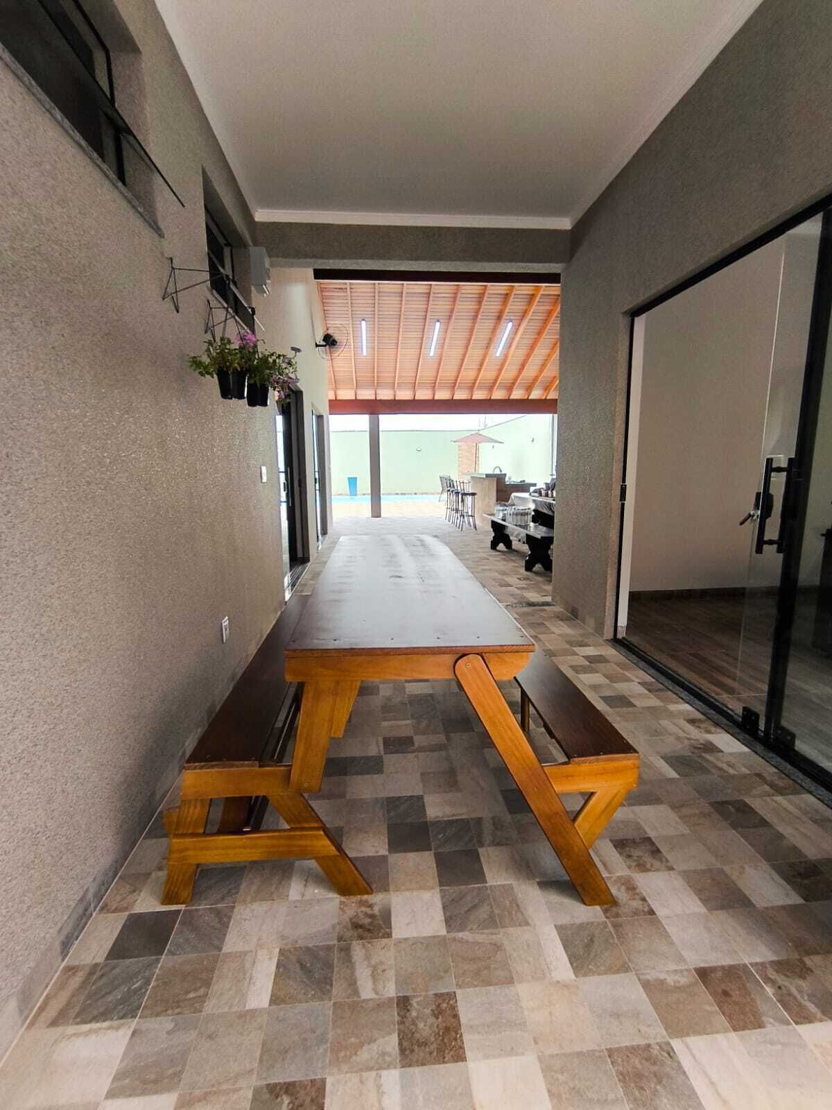 Ein Korridor mit einer langen Holzbank, einem Fliesenboden und Blick auf einen Außenbereich mit Tisch und Stühlen.