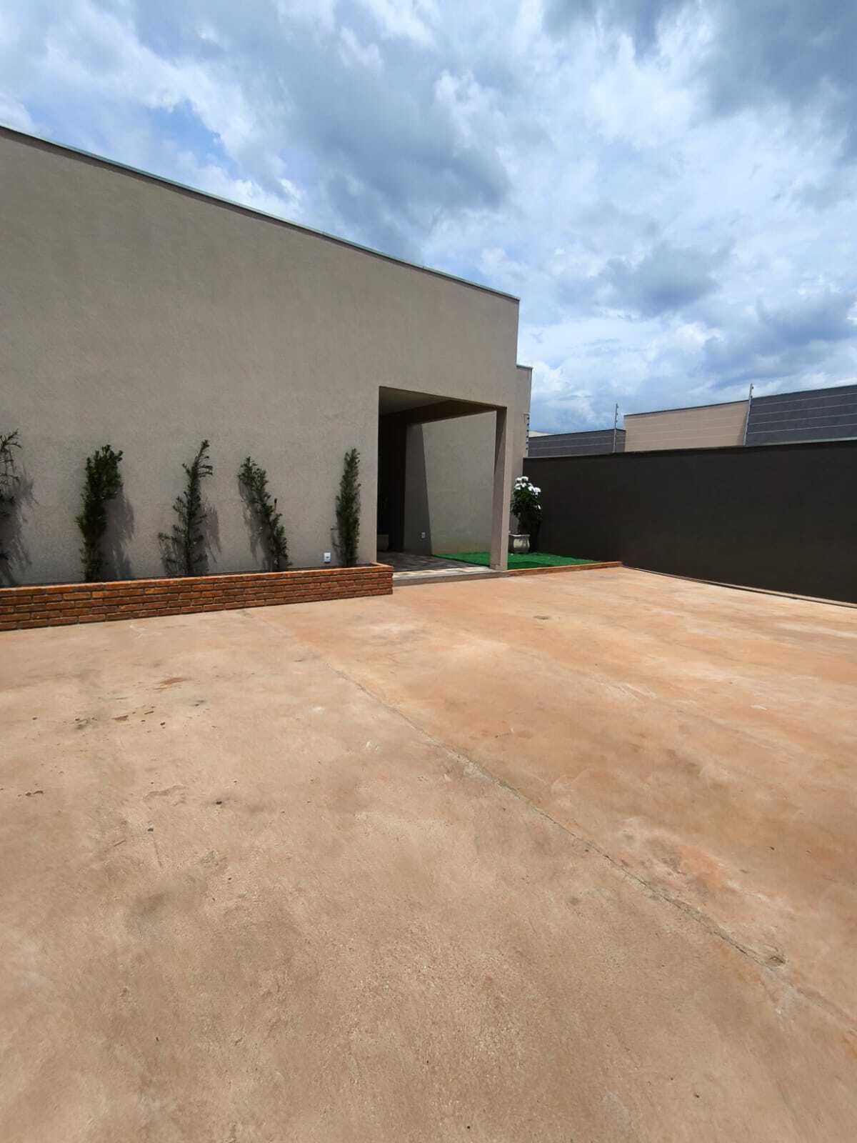 Un edificio moderno con techo plano, patio de hormigón y un pequeño jardín con plantas en macetas.