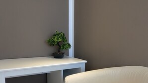 A white desk with a small potted plant and a white chair in a room with a brown wall and wooden flooring.