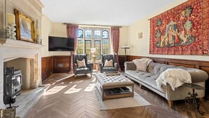 A spacious living room with a fireplace, a large tapestry, and a comfortable seating area. - Historic House in Bourton on the Water (Bourton-on-the-Water)