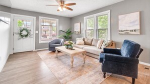 A spacious living room with a wooden floor, a ceiling fan, a sofa, a chair, and a coffee table. - Charming Downtown Harrison Home (Harrison)