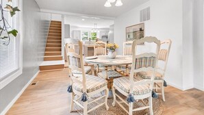 A dining area with a round table, white chairs with plaid cushions, and a chandelier. - Charming Downtown Harrison Home (Harrison)