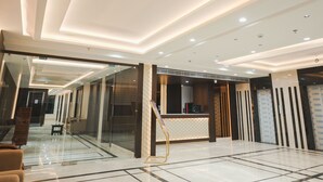 A modern hotel lobby with a reception desk, glass partitions, and a patterned wall. - Hotel Raghukul Grand (Azamgarh)