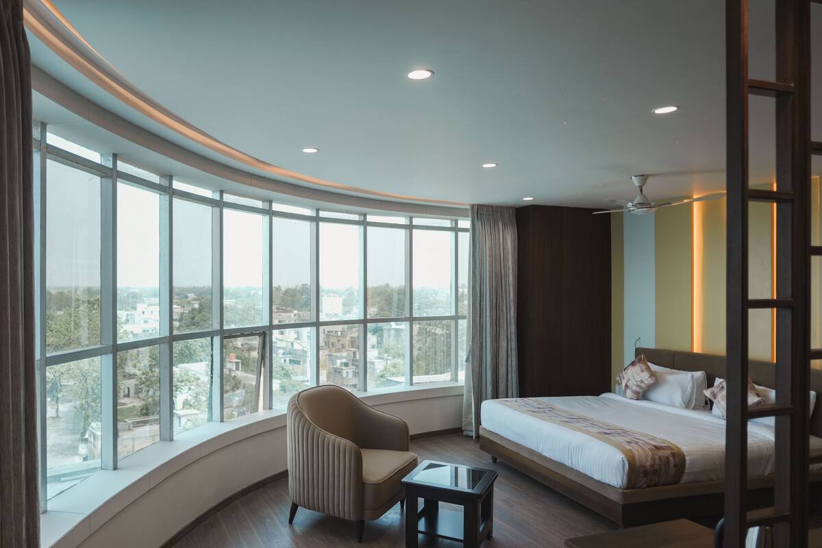 A hotel room with a curved window, a bed, a chair, and a small table.