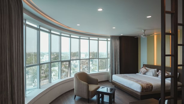 A hotel room with a curved window, a bed, a chair, and a small table. - Hotel Raghukul Grand (Azamgarh)