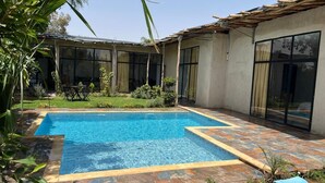 A rectangular swimming pool with a tiled border, surrounded by a patio area with stone tiles and a grassy lawn. - Family villa, private pool, not overlooked (Marrakech)