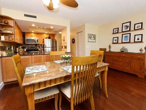 A dining area with a wooden table and chairs, a kitchen in the background, and a wall with framed pictures. - Walk to St. Augustine Beach | Poolside Patio (St. Augustine)