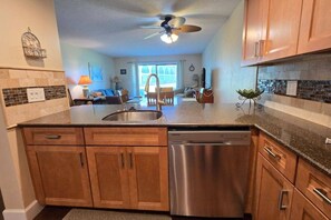 A modern kitchen with wooden cabinets, a stainless steel dishwasher, and a ceiling fan. - Walk to St. Augustine Beach | Poolside Patio (St. Augustine)