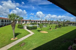 En hotellinnergård med en pool, palmer och en byggnad med välvda fönster.