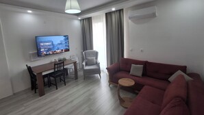 Ein modernes Wohnzimmer mit Flachbildfernseher, einem Esstisch, einem roten Sofa, einem grauen Sessel und einem kleinen Holztisch.