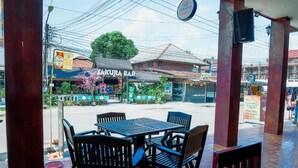 Un'area esterna con tavoli e sedie, un cartello con la scritta "TAKURA BAR" sullo sfondo e vista sulla strada con edifici e linee elettriche.