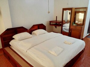 A neatly made bed with white linens and pillows, a wooden nightstand, a mirror, and a small wooden dresser with a mirror.