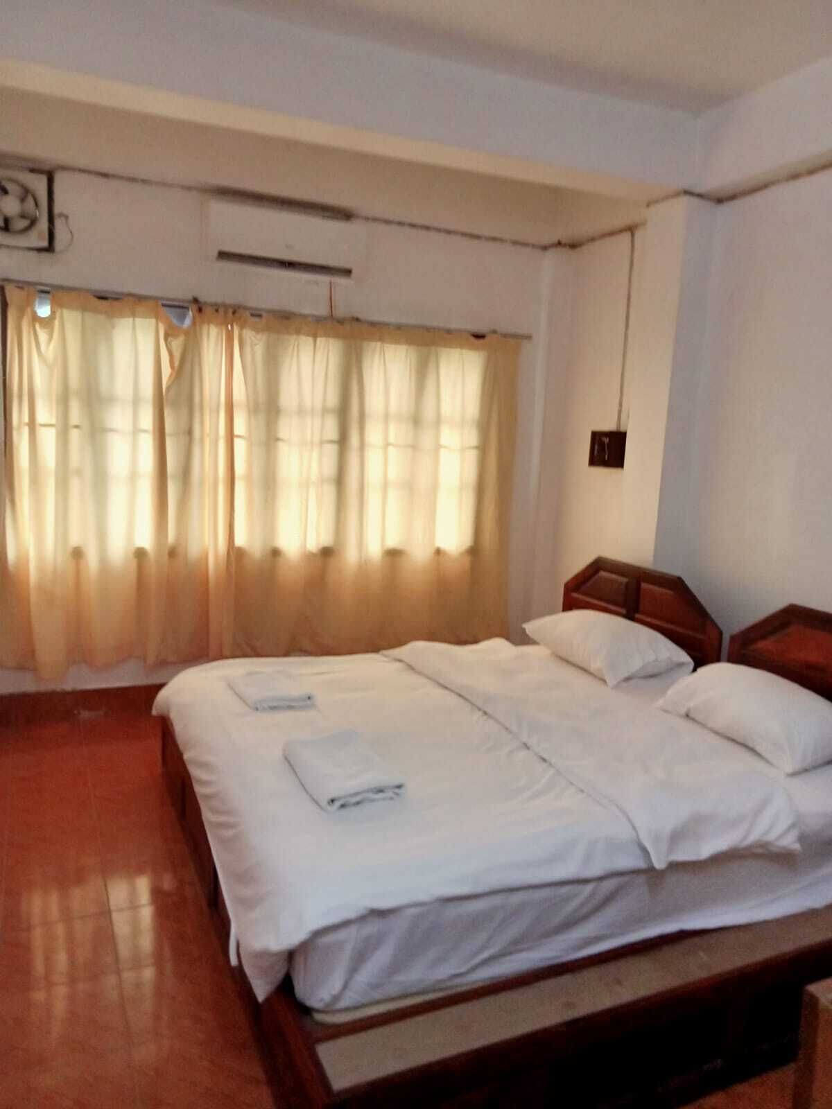A hotel room with a large bed, a wooden headboard, and a window with curtains.