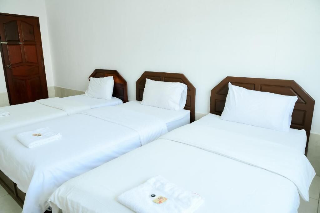Habitación de hotel con tres camas individuales, cada una con cabecero de madera y ropa de cama blanca.