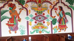 Un interno ristorante con tavoli e sedie in legno, un murale con opere d'arte culturali e un pavimento piastrellato.