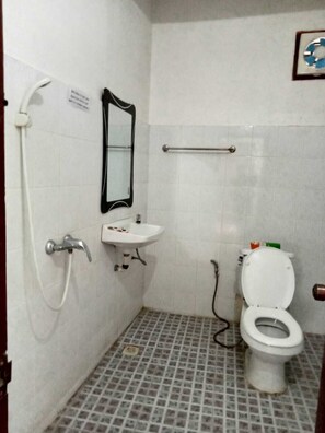 A small, tiled bathroom with a white sink, a mirror, a toilet, and a shower.