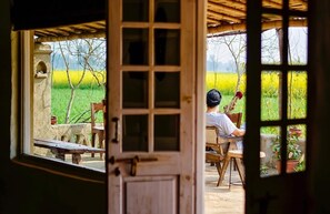 Une porte en bois rustique, dotée d’une fenêtre, donne sur un espace extérieur aménagé avec une table et des chaises, et offre une vue sur un champ.