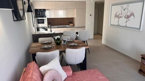 Un comedor moderno con una mesa de madera preparada para cuatro personas, sillas grises tapizadas y un sofá rosa con cojines.