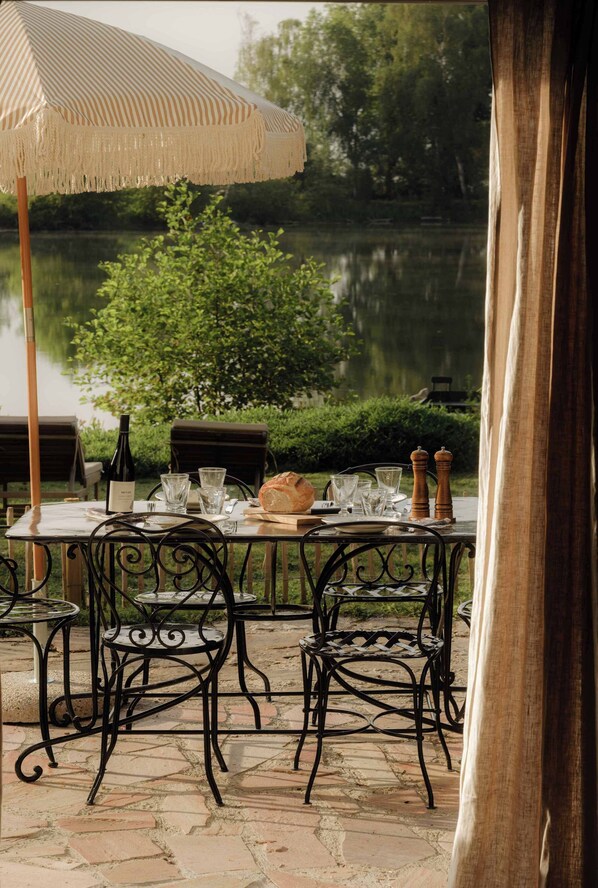 Un área de comedor al aire libre con una mesa para dos, una botella de vino y una hogaza de pan.