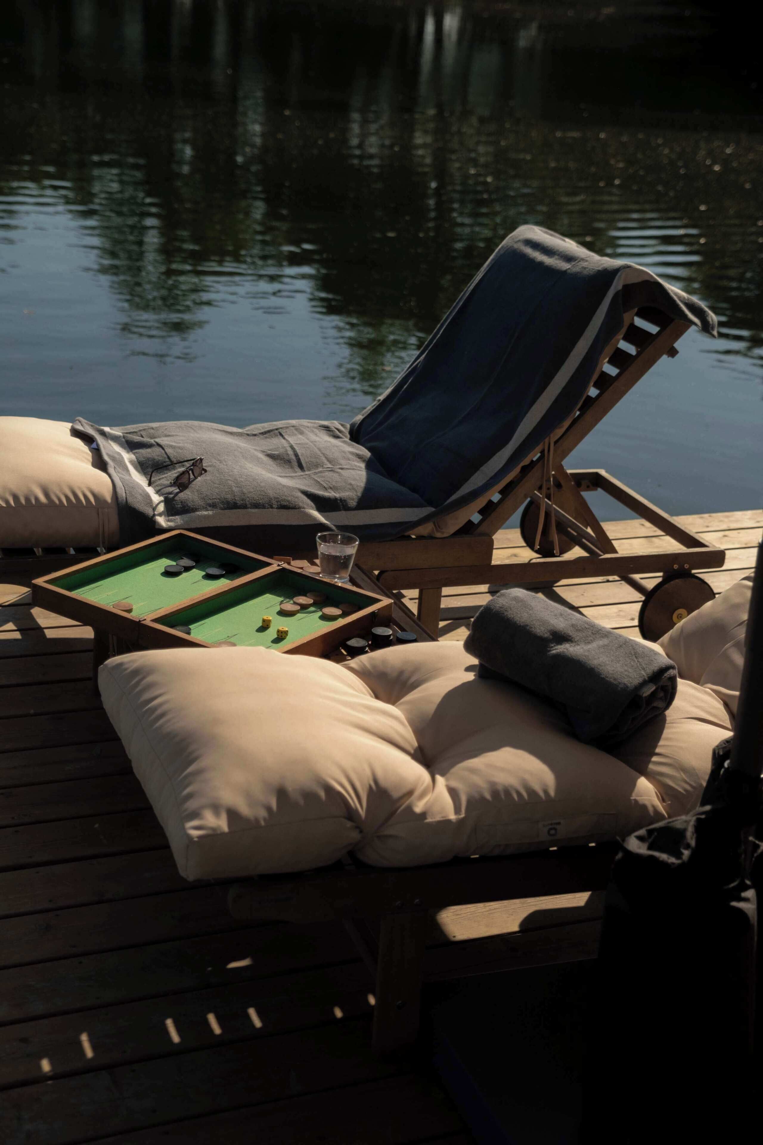 A deck with a pool table, lounge chairs, and cushions.
