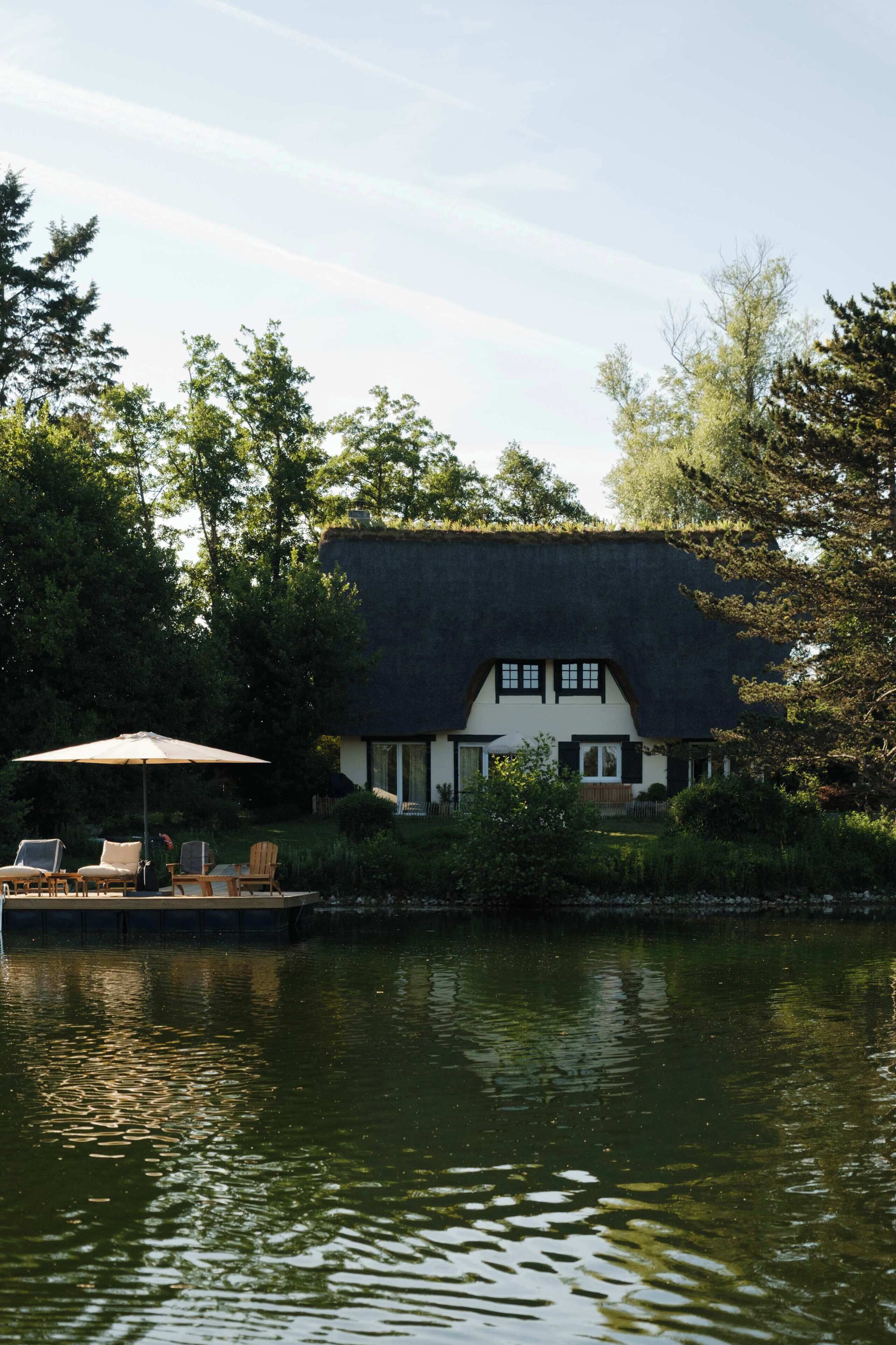 Een huis met rieten dak, gelegen aan het water, met terras en buitenmeubilair.