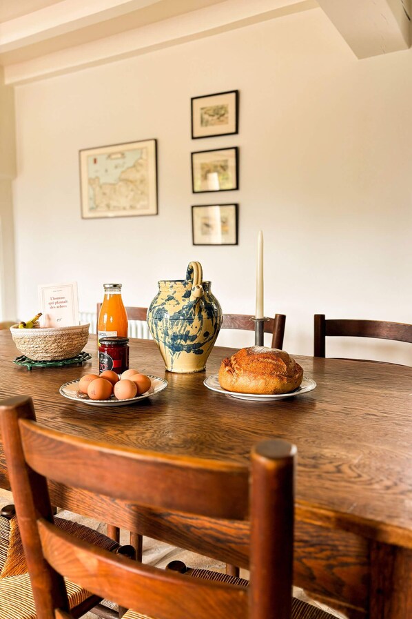 A wooden dining table with a plate of eggs, a loaf of bread, a bottle of orange juice, a vase, and a candle.