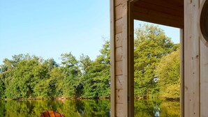 Un pontile in legno con una sedia e un tavolo di legno, con vista su un lago calmo e alberi sullo sfondo.