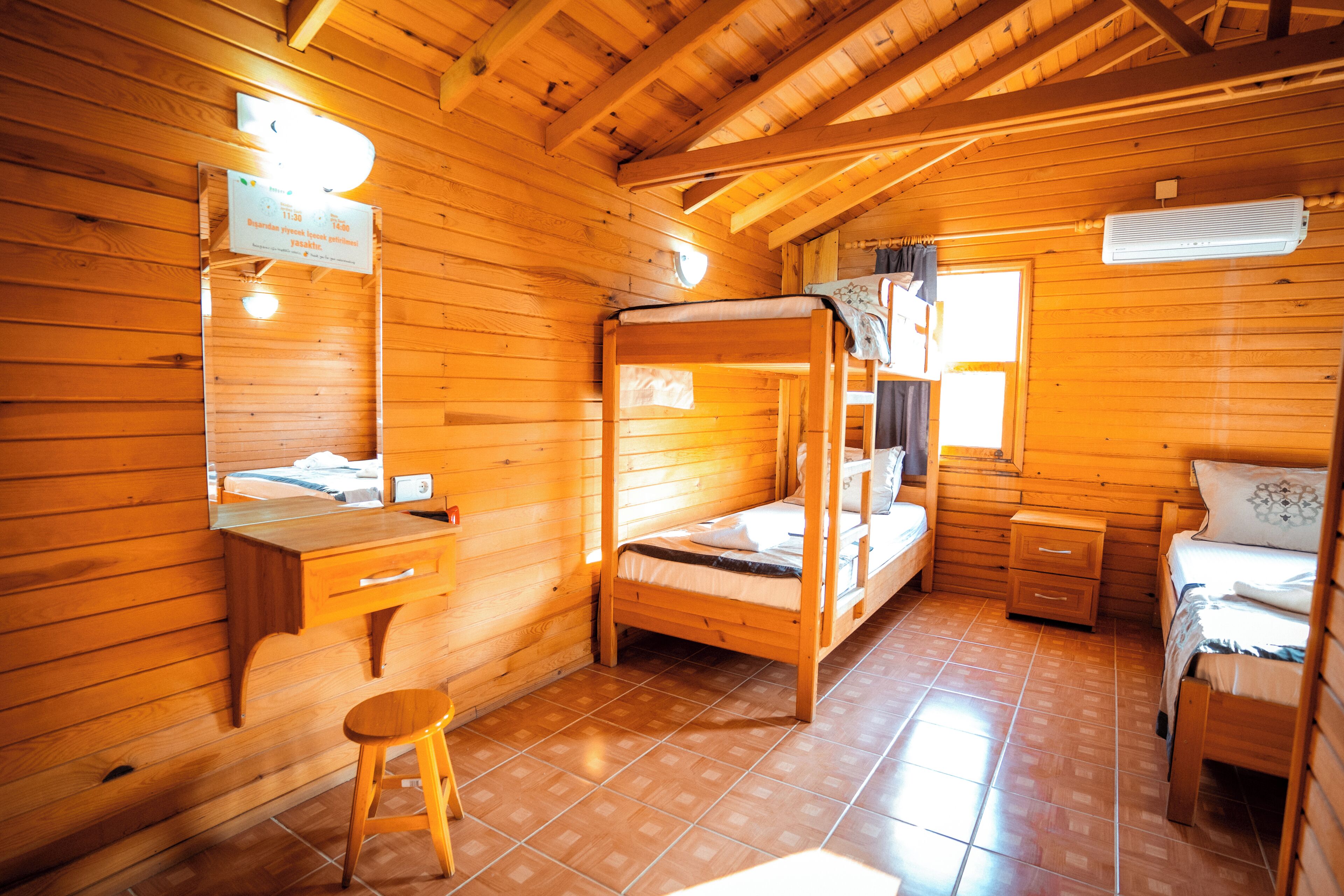 A wooden cabin room with a bunk bed, a desk, a chair, and a window.