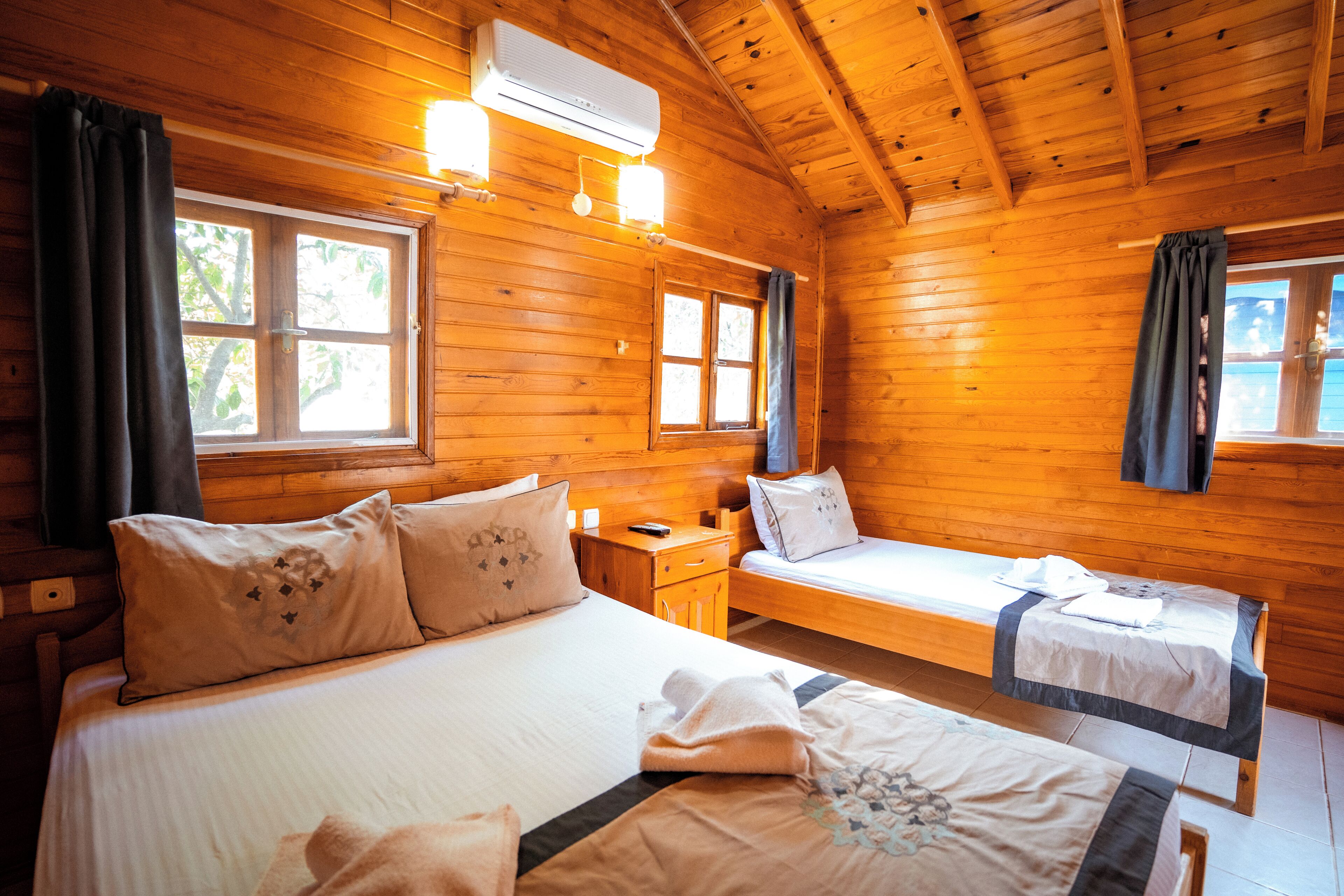 Quarto de cabana de madeira com duas camas, uma mesa de cabeceira e um aparelho de ar condicionado.