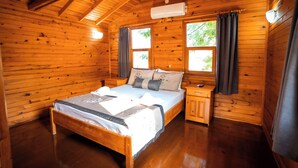 A wooden cabin bedroom with a bed, nightstands, and a window with curtains. - Portakal Bahçesi Bungalow (Kumluca)