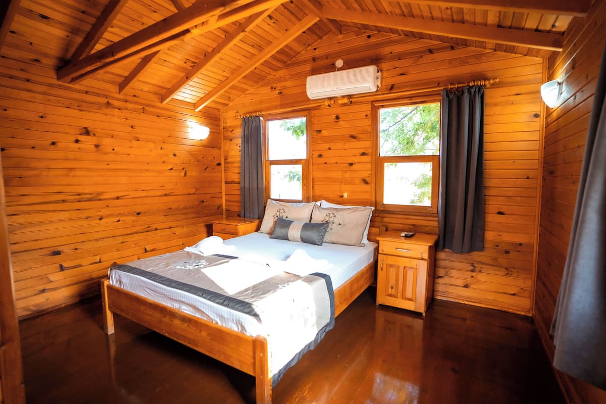 Ein Schlafzimmer einer Holzhütte mit einem Bett, Nachttischen und einem Fenster mit Vorhängen.