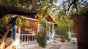 A wooden cabin with a porch, surrounded by gravel and trees. - Portakal Bahçesi Bungalow (Kumluca)