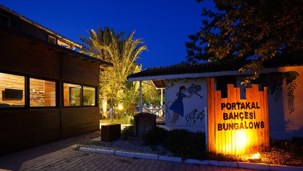 A wooden building with a sign reading "PORTAKAL BAHÇESI BUNGALOWS" and a mural of a person watering plants. - Portakal Bahçesi Bungalow (Kumluca)