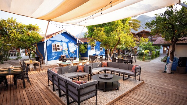 An outdoor patio area with wooden flooring, a sectional sofa, and a round table. - Portakal Bahçesi Bungalow (Kumluca)
