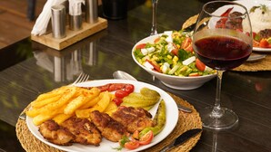 A plate of food with fries, a salad, and a glass of red wine on a table. - Portakal Bahçesi Bungalow (Kumluca)