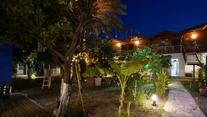 Un edificio de madera con un sendero de piedra, asientos al aire libre y un árbol con luces colgantes.
