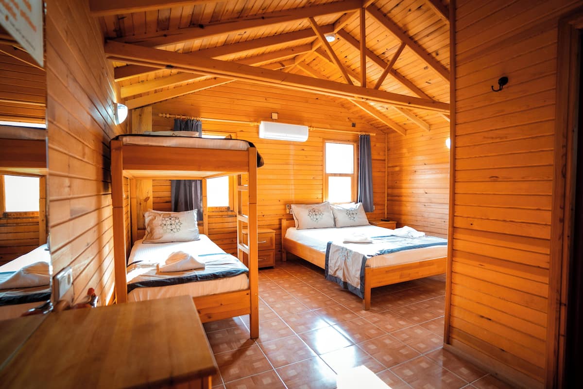 Eine Holzhütte mit drei Etagenbetten, einem kleinen Tisch und einem Fenster mit Vorhängen.