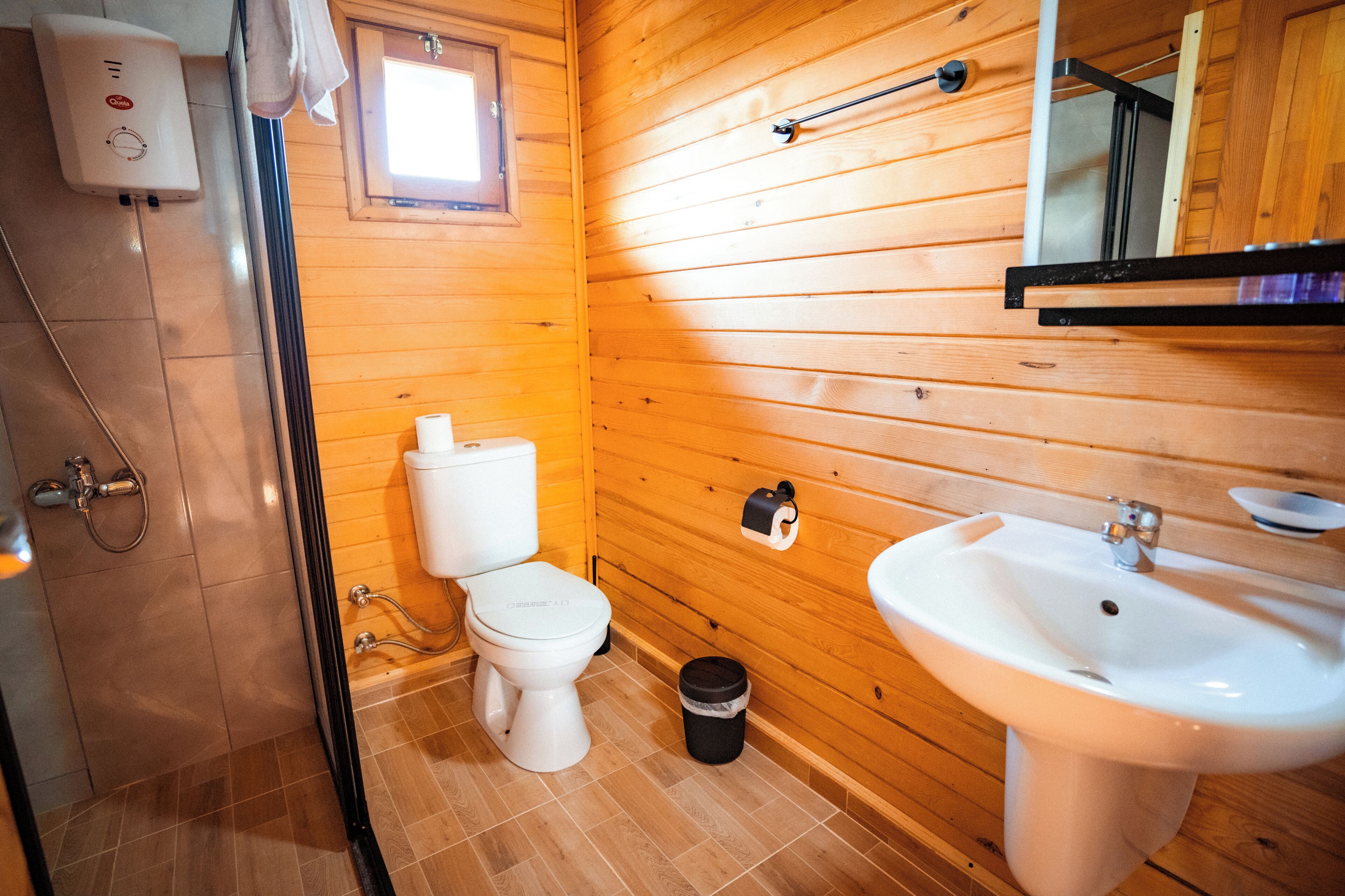 Un bagno con rivestimenti in legno, dotato di WC, lavabo e doccia.