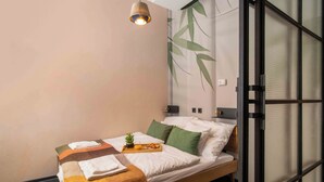 A modern bedroom with a bed, a bedside table, a wall-mounted lamp, and a large window with a view of greenery. - ASTORIA Loft Elite Apartment free parking,AC,Elevator (Budapest)