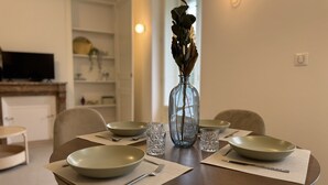 Et spisebord dækket med tallerkener, bestik og glas, med en vase med tørrede blomster i midten.
