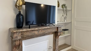 En moderne stue med et fladskærms-tv på en marmorpejsmantel, en mørk vase med visne blomster og en hvid dør.