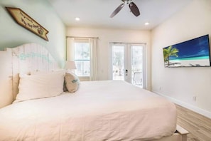 A bedroom with a bed, a ceiling fan, a painting of a beach, and a sign on the wall.