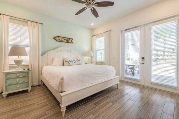 A bedroom with a bed, nightstands, a ceiling fan, and large windows.