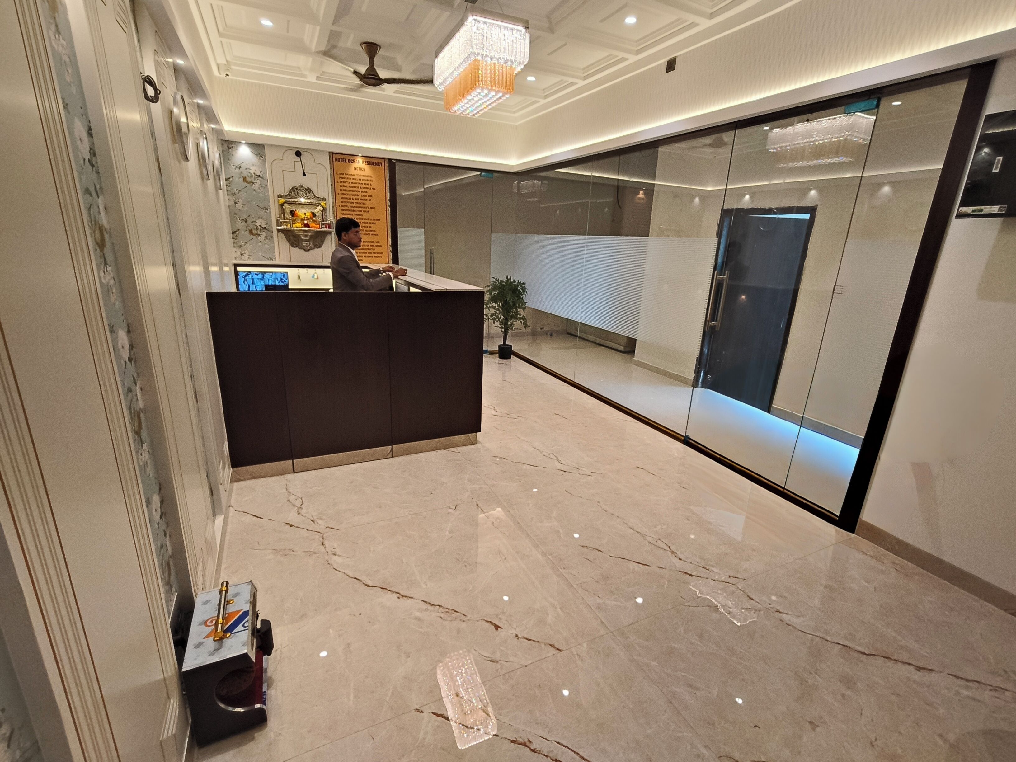 Ein Hotel-Empfangsbereich mit Marmorboden, einem Empfangstresen, einer Chandelierleuchtre und einer Glastrennwand.