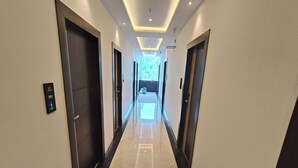 A modern hotel hallway with a marble floor, dark doors, and a ceiling with recessed lighting.